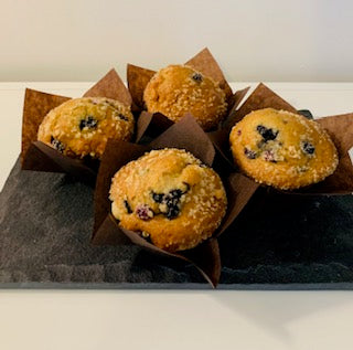 Four large bakery-style blueberry muffins with golden, domed tops and bursts of baked blueberries, arranged neatly on a serving platter.