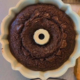 A whole, dense chocolate pound cake with a deep cocoa color, displayed on a simple cake stand for an elegant presentation.